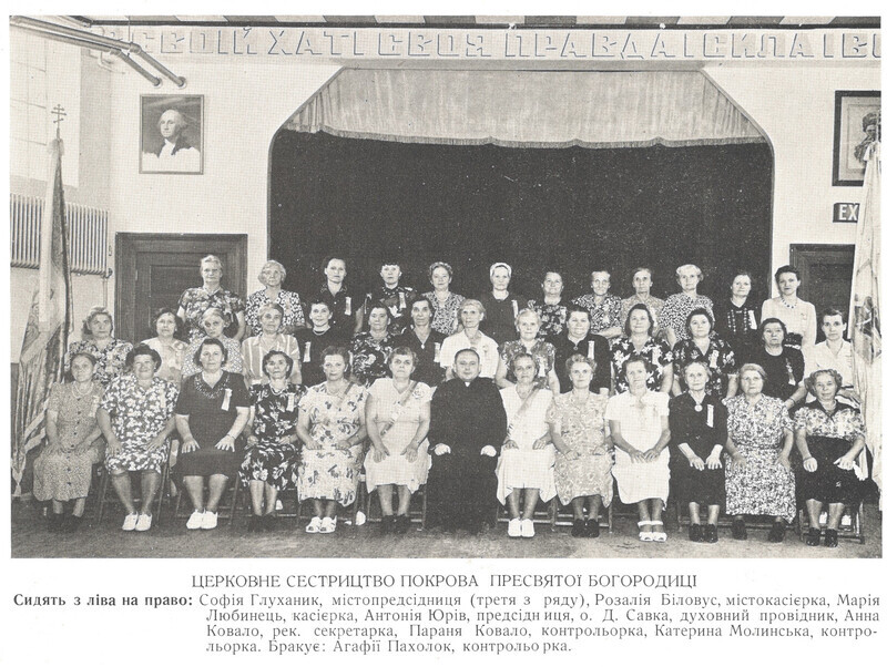 Photograph is undated, but likely 1948. Caption translation (names transliterated using Library of Congress standard): "Church Sisterhood of the Protection of the Mother of God ['Pokrova']", "Sitting from left to right: Sofia Hlukhanyk, vice president (third in the row); Rozaliia Bilovus, assistant treasurer; Maria Liubynets', treasurer; Antoniia Iuriv, president; Fr. D. Savka, spiritual leader; Anna Kovalo, recording secretary; Parania Kovalo, auditor; Kateryna Molyns'ka, auditor. Missing: Ahafiia Pakholok, auditor."